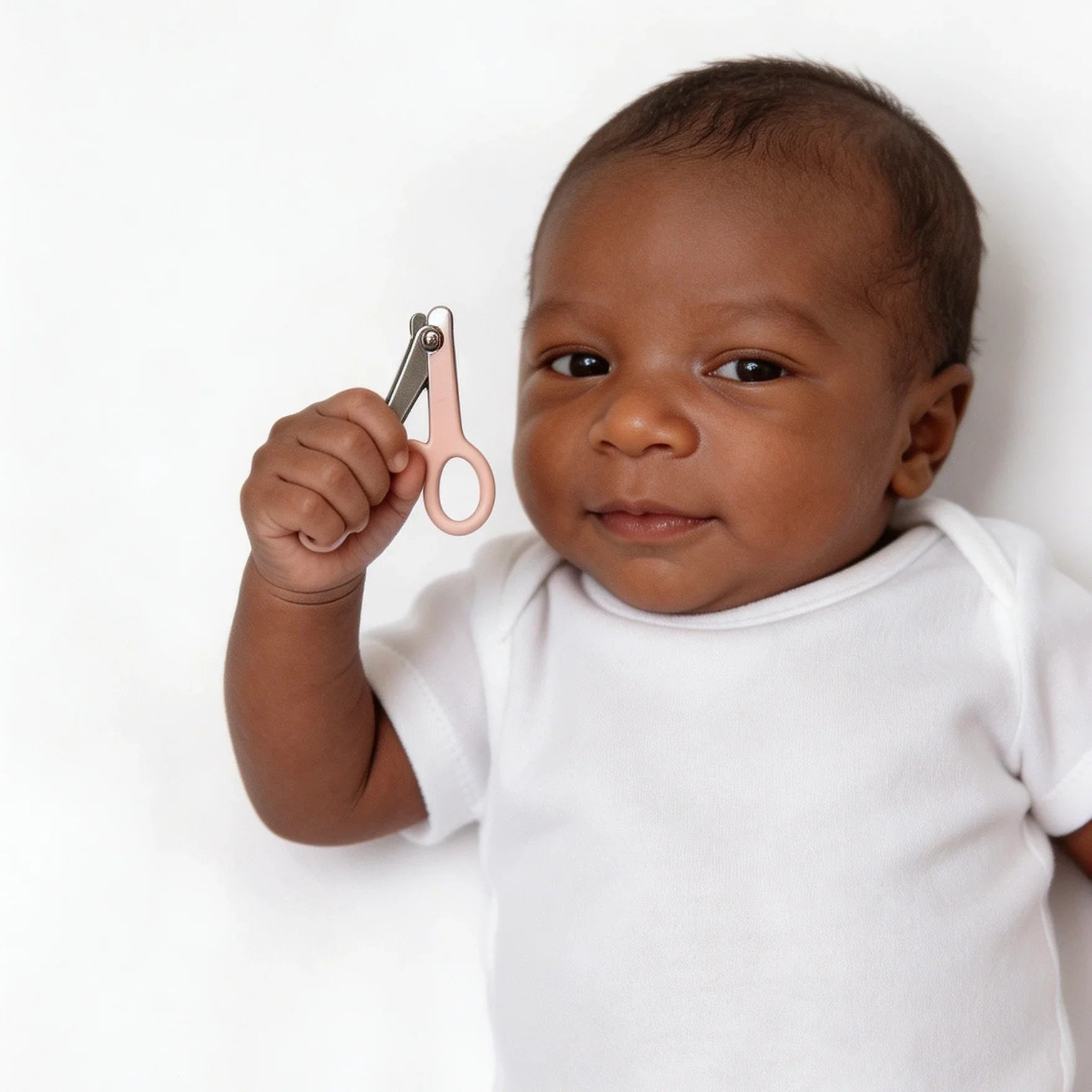 Smiling baby in white holding pink-handled nail clippers against white background
